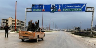 Syrian army soldiers gesture on the highway outside Maarat al-Numan